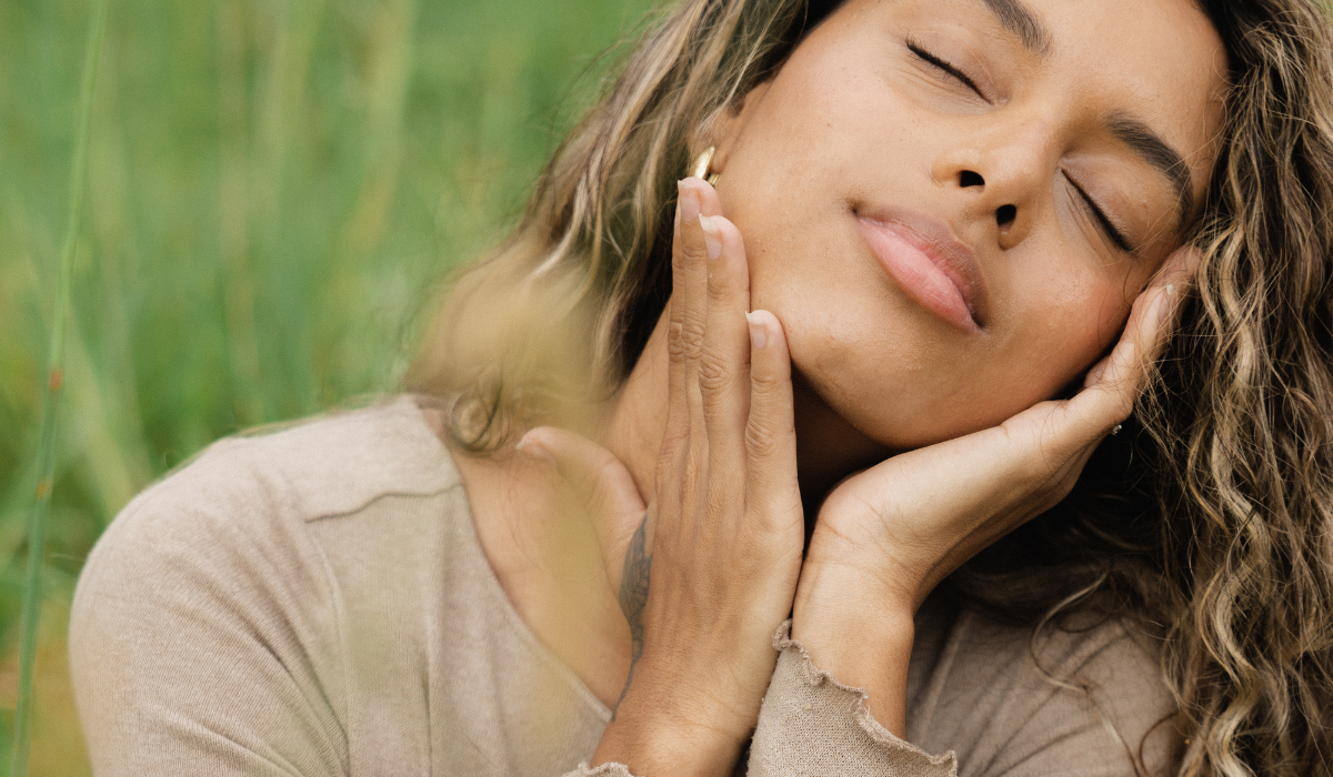 A lady sitting in a field of grass holding her hands on her face